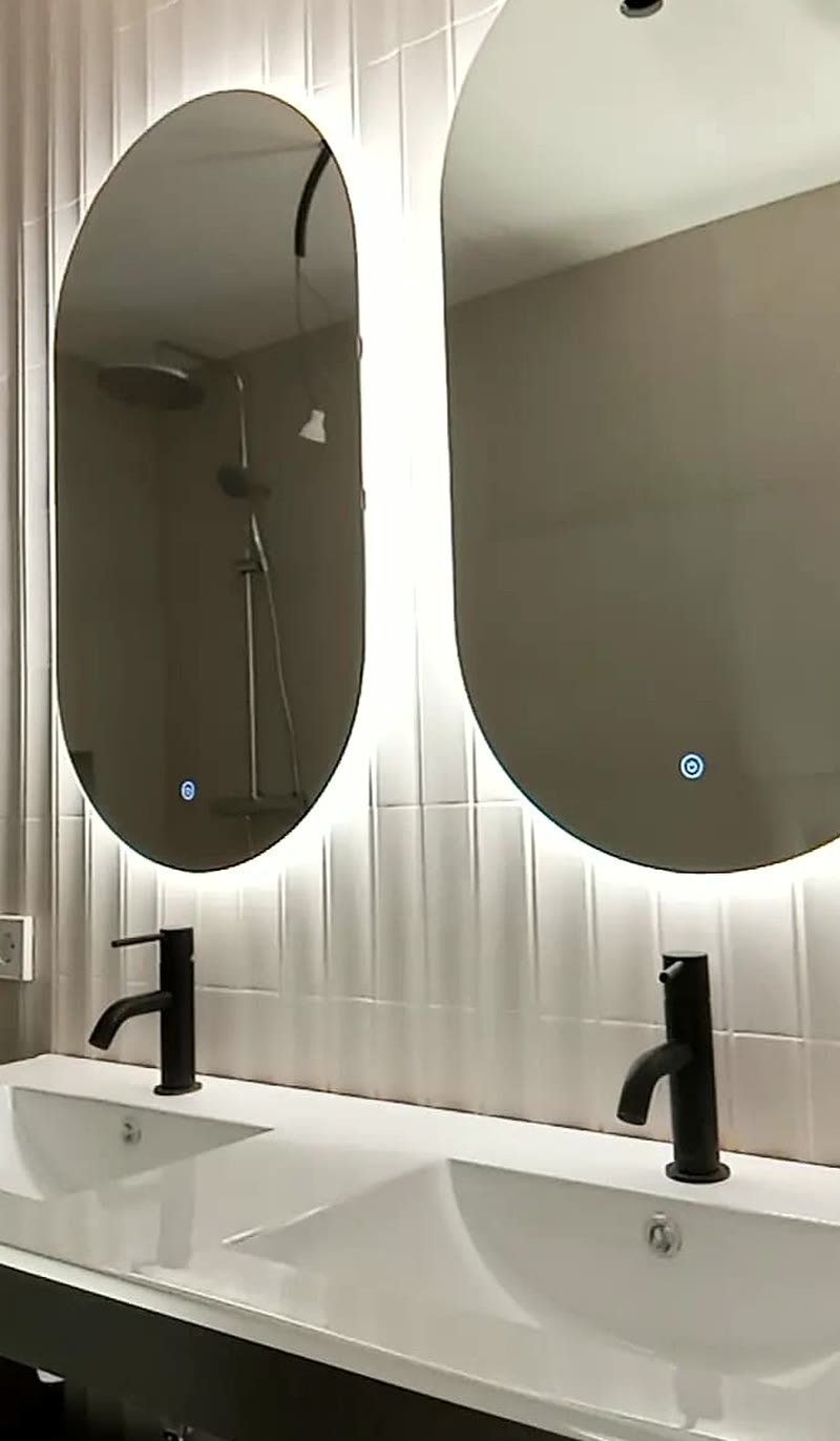 Espejos ovalados retroiluminados sobre doble lavabo con grifería negra